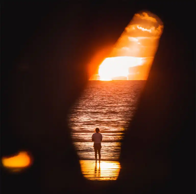 A person standing on the beach looking at the sunset